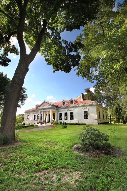a large white house with a tree in the yard at Dwór Bieganów in Bieganów