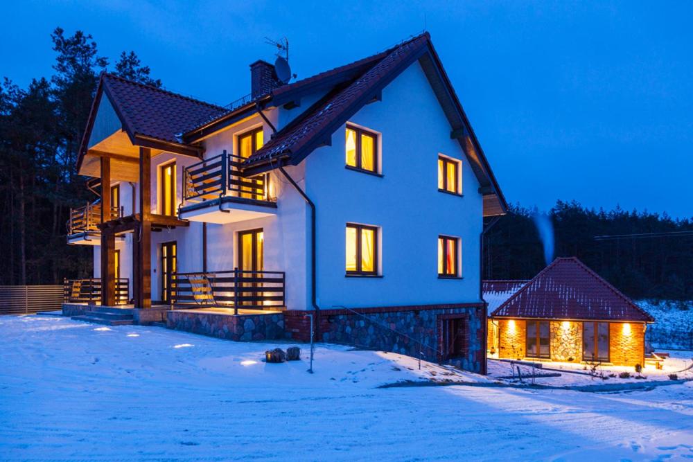 una casa con luces encendidas en la nieve en Gościniec Krutyński en Krutyń