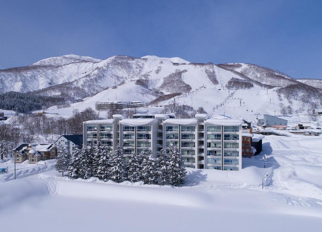 un bâtiment dans la neige avec des montagnes en arrière-plan dans l'établissement Niseko Landmark View, à Niseko