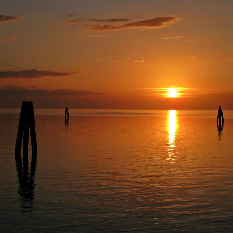 a sunset over the water with poles in the water at Locanda Stravedo in Pellestrina