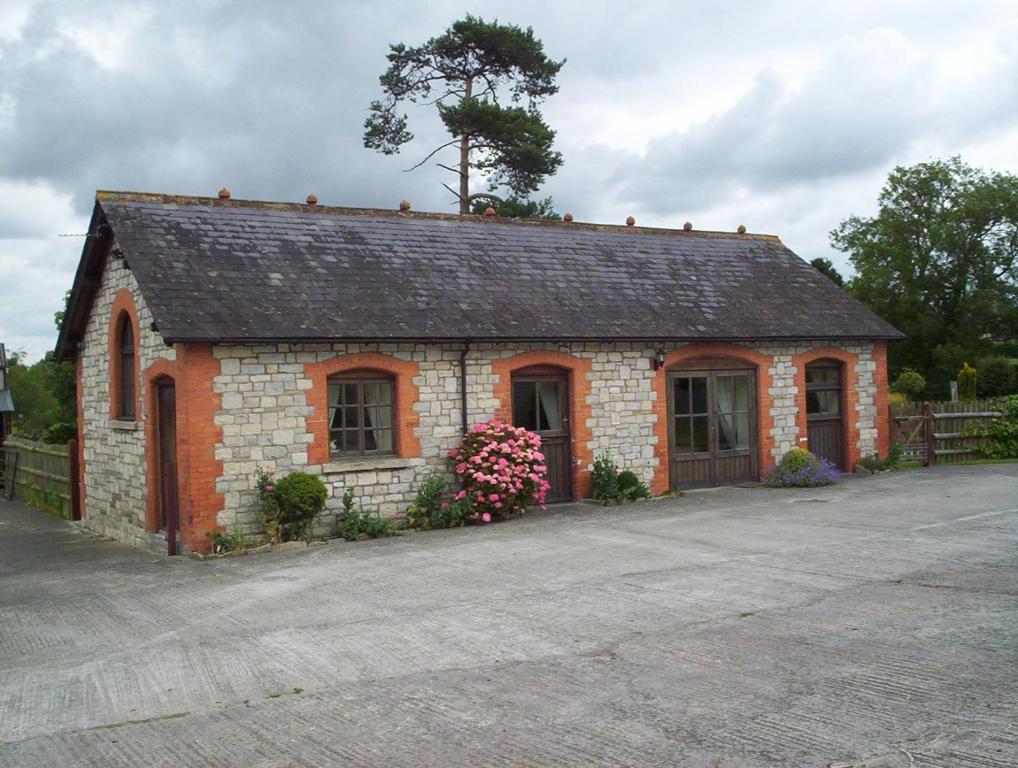 un petit bâtiment en briques avec des fleurs devant lui dans l'établissement The Stables, à South Barrow