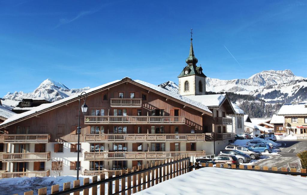 een groot gebouw met een klokkentoren in de sneeuw bij Résidence Odalys Le Village in Notre-Dame-de-Bellecombe