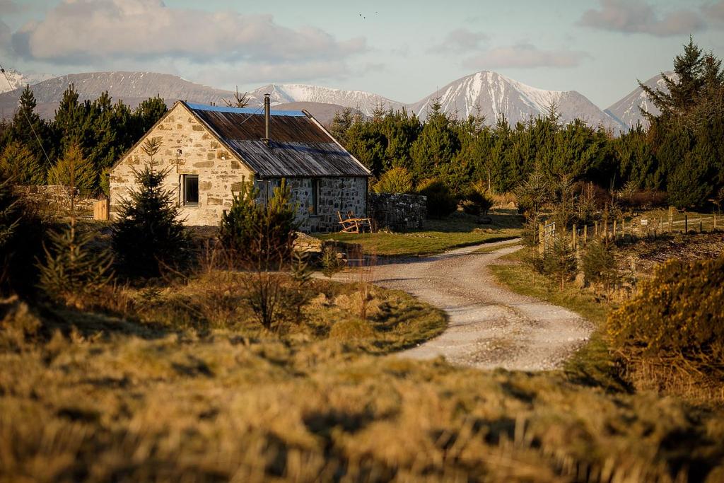 an old house in a field with mountains in the background at Lusa Bothy in Lusa