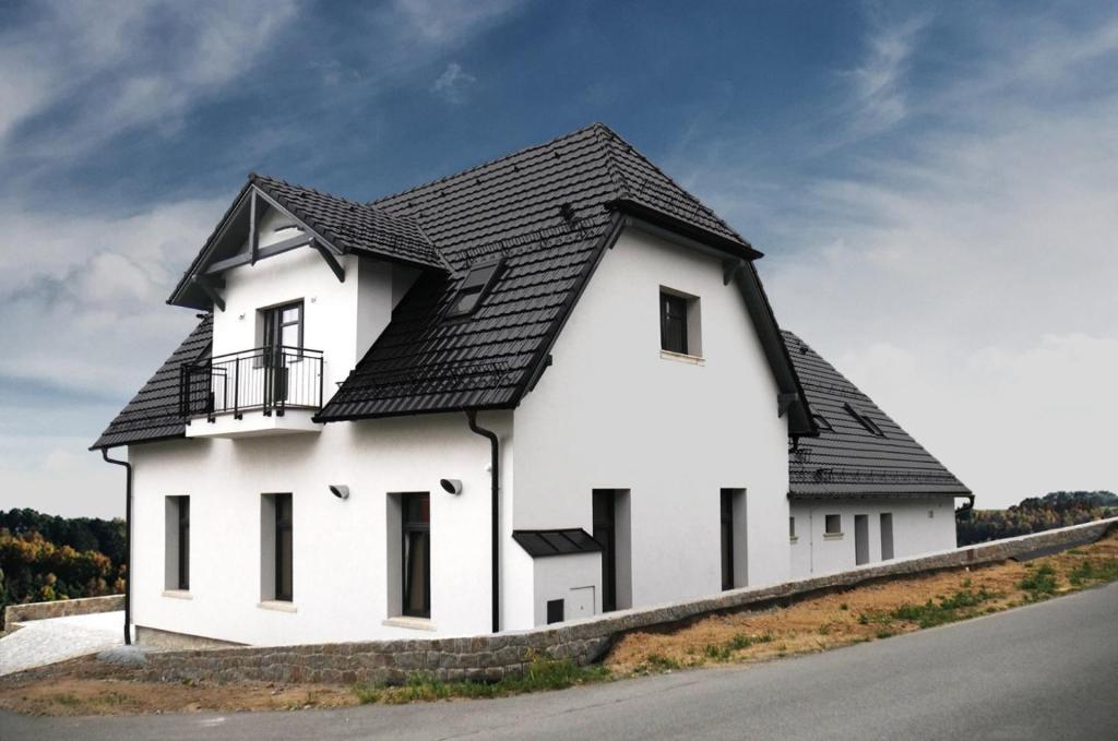 a white house with a black roof on the side of a road at Penzion Na Zlaté cestě in Tachov