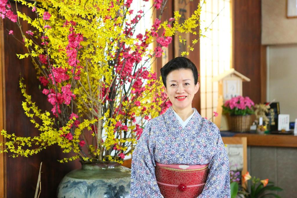 Una donna in piedi accanto a un vaso di fiori di Ogiwarakan a Chikuma