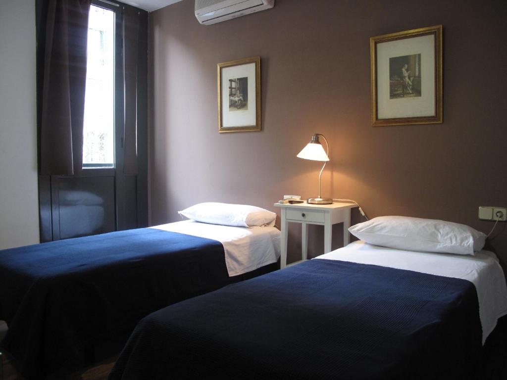 a room with two beds and a table with a lamp at Hostal LK Barcelona in Barcelona