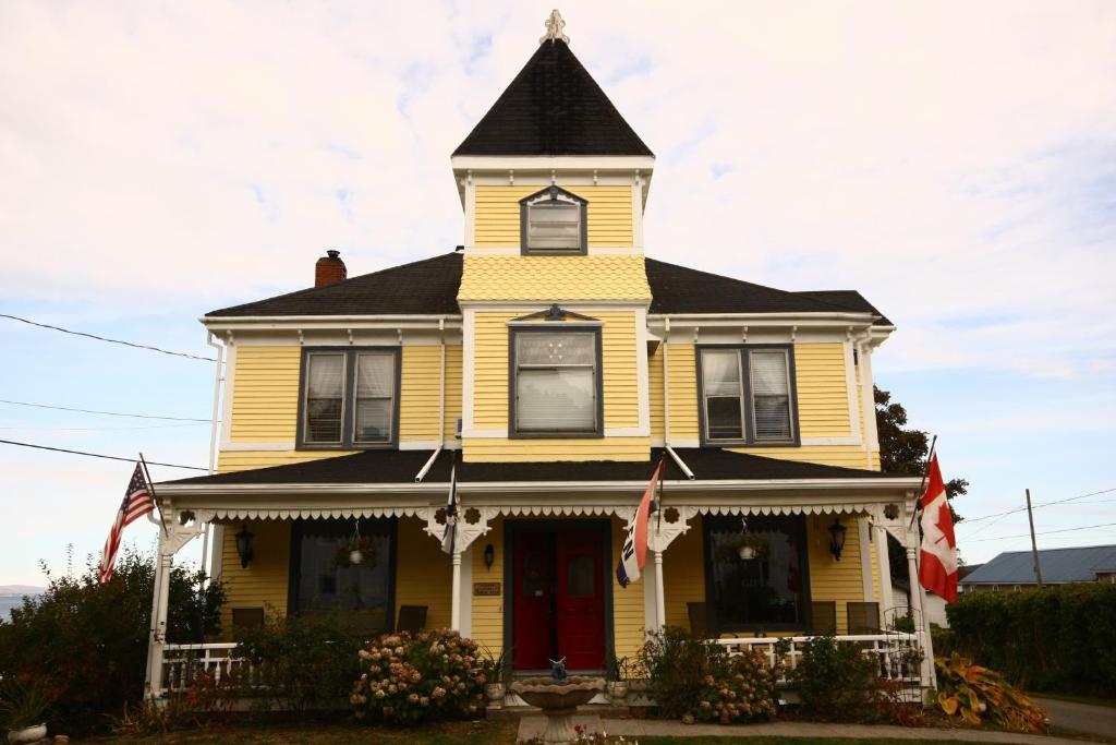 a yellow house with a black roof and a red door at Come from Away B&B in Digby