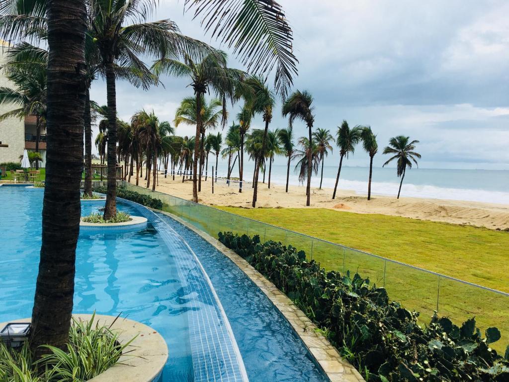 a resort swimming pool with palm trees and the beach at Wai Wai Cumbuco Apartamento Térreo in Cumbuco