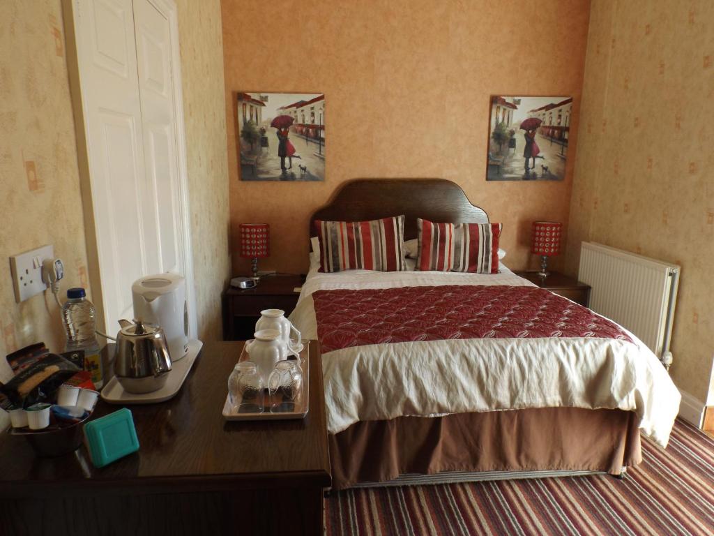 a bedroom with a bed with a desk and two pictures on the wall at Rosedene Guest House in Pembroke