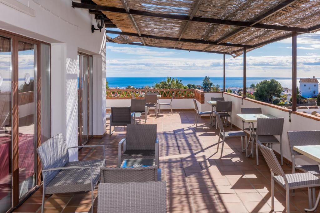 Un patio con mesas y sillas y el mar. en Hotel Rural Almazara, en Frigiliana