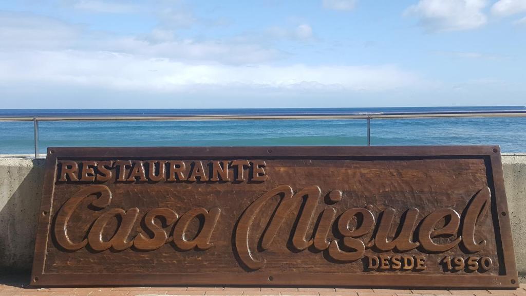 um sinal para um restaurante chamado casa albuquerque com o oceano em Pensión Casa Miguel em Artedo