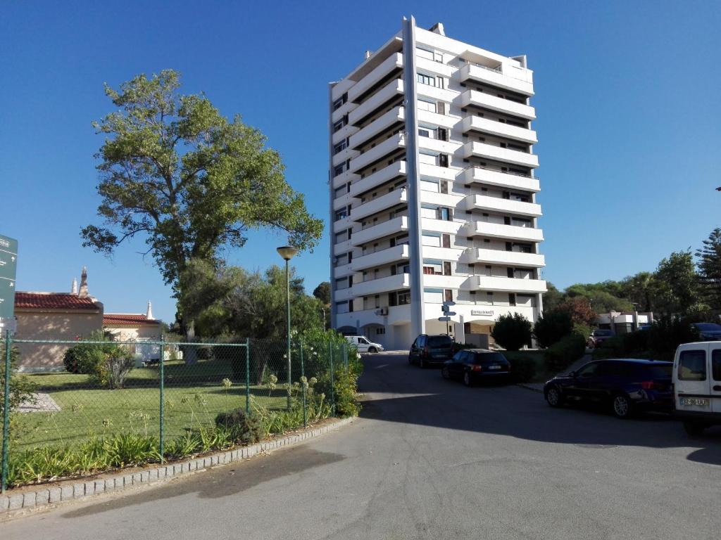 een groot wit appartementencomplex naast een parkeerplaats bij Apartamento Alvor in Alvor