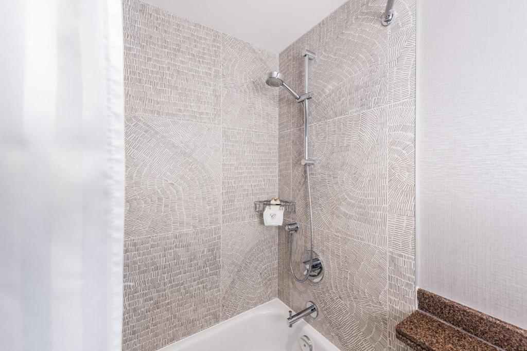 a bathroom with a shower with a white tub at Carmana Hotel & Suites in Vancouver