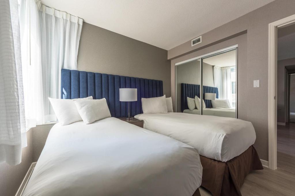 two beds in a hotel room with a mirror at Carmana Hotel & Suites in Vancouver