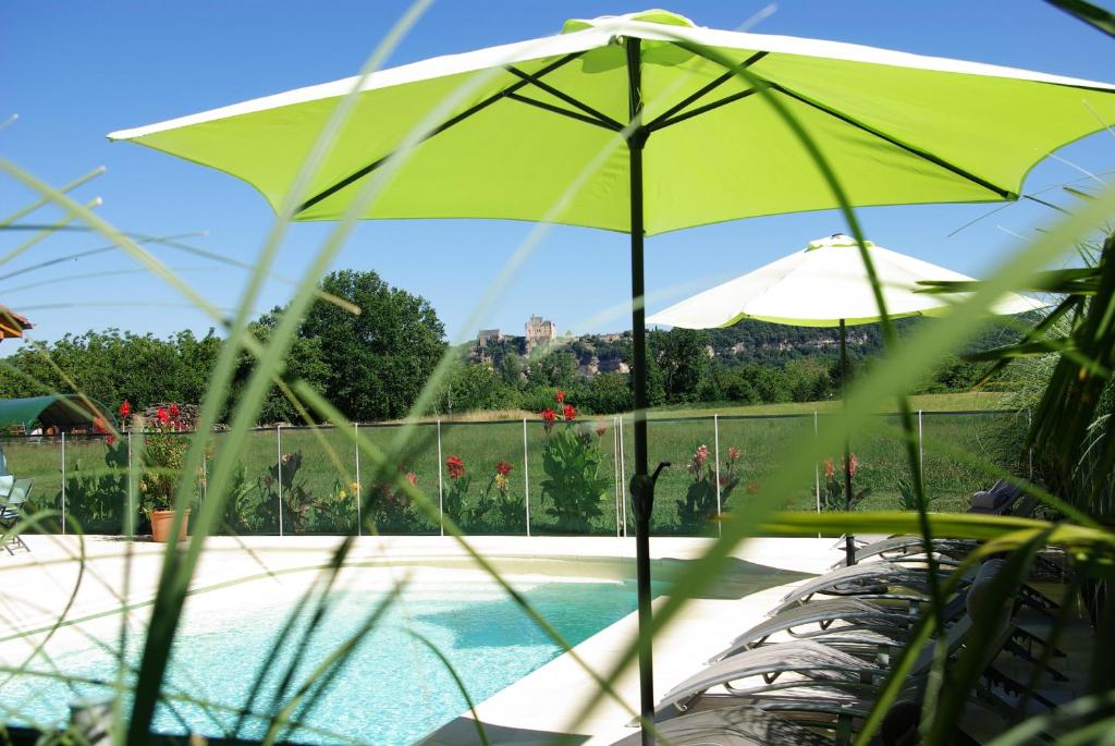 - un parasol vert à côté de la piscine dans l'établissement chez gallon chambres d’hôtes, à Vézac