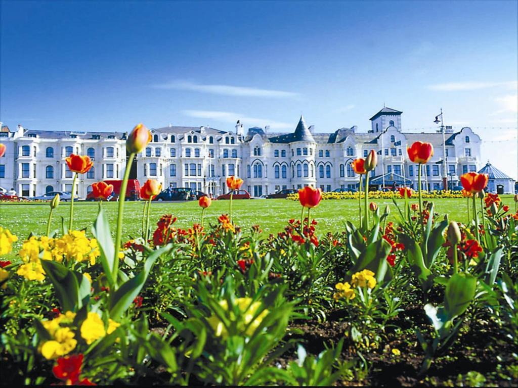 un grand bâtiment avec un champ de fleurs devant lui dans l'établissement Royal Clifton Hotel, à Southport