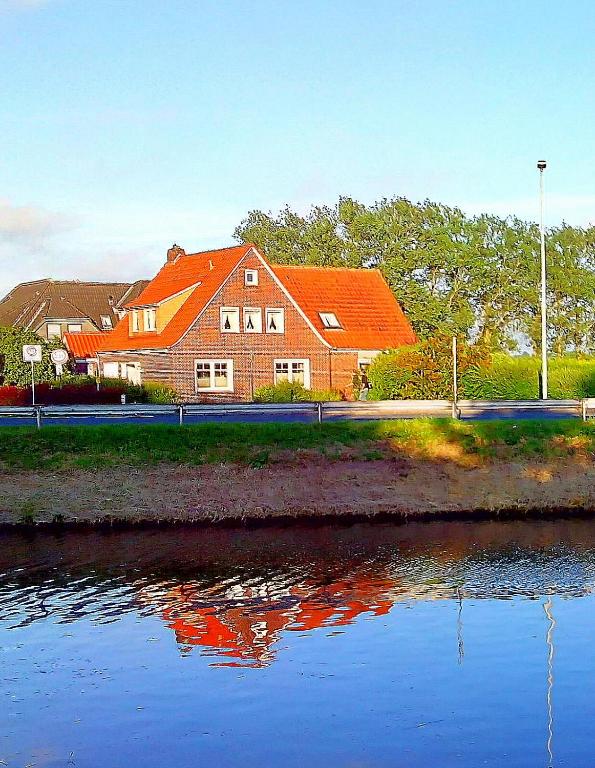 a house with an orange roof next to a body of water at Ferienwohnung Deichstr De Lorenzo in Carolinensiel