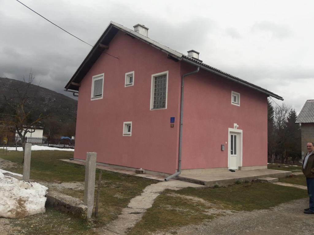 a red house with a man standing in front of it at Apartment Jopa in Korenica