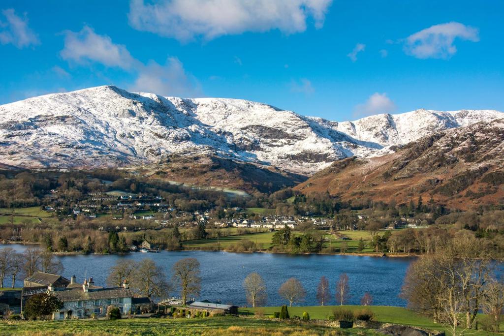 a village on the shore of a lake with snow covered mountains at Bank Ground Farm in Coniston