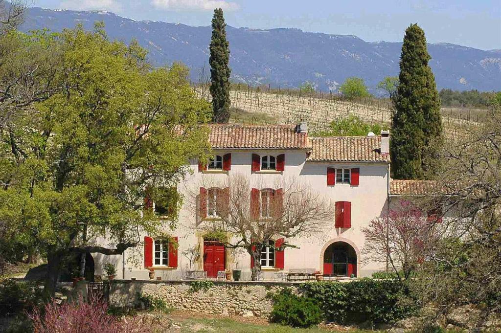 ein großes weißes Haus mit roten Türen und Bäumen in der Unterkunft La Tuilière en Luberon in Cadenet