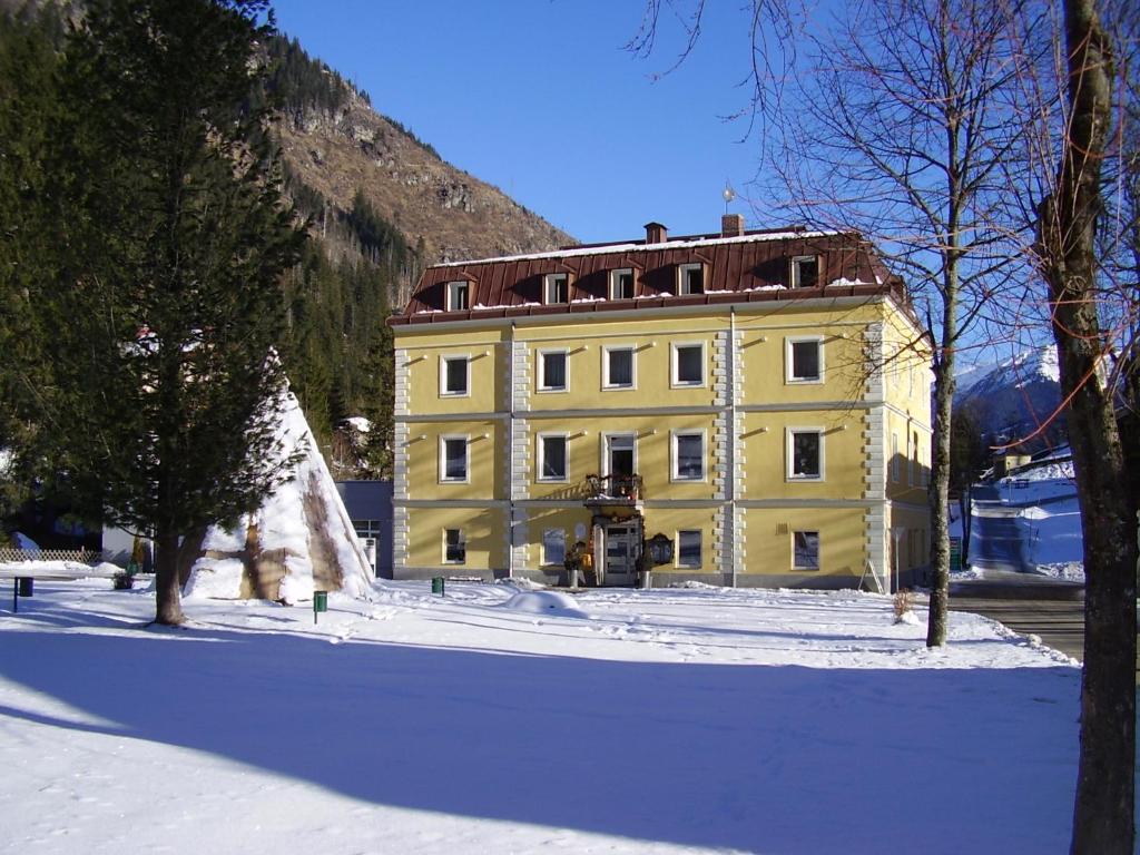 żółty budynek w śniegu przed górą w obiekcie Hotel Rader w mieście Bad Gastein