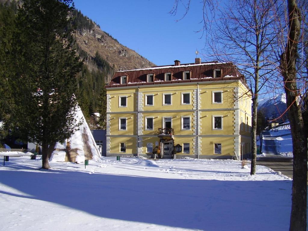 een geel gebouw in de sneeuw voor een berg bij Hotel Rader in Bad Gastein