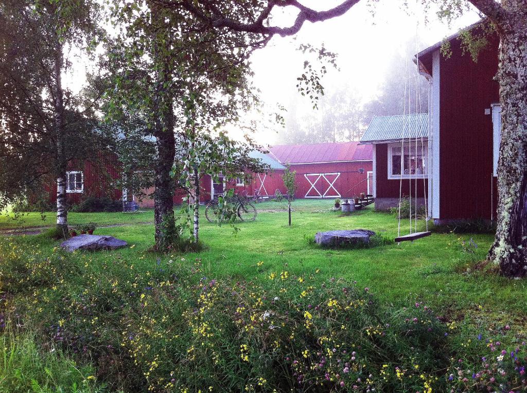 une grange rouge avec une cour plantée d'arbres et de fleurs dans l'établissement Olo Tila, à Kurikka