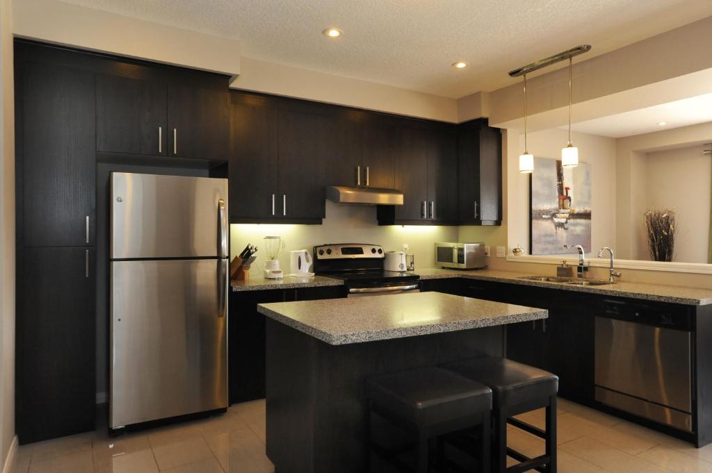 cocina con armarios negros y nevera de acero inoxidable en Boardwalk Homes Executive Guest Houses, en Kitchener