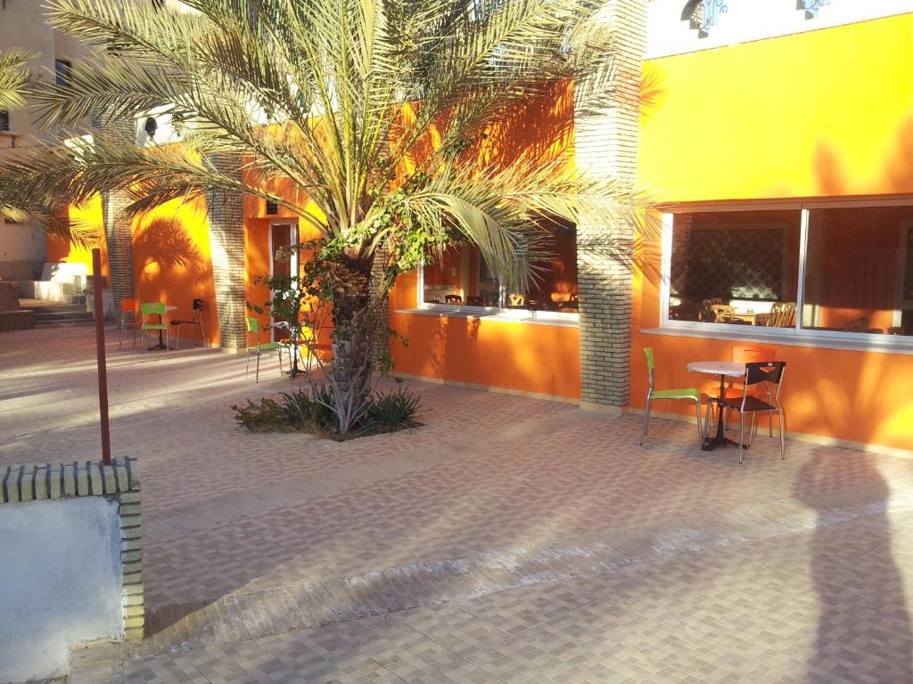 a palm tree in front of a building with a table and chairs at Résidence El Arich in Tozeur