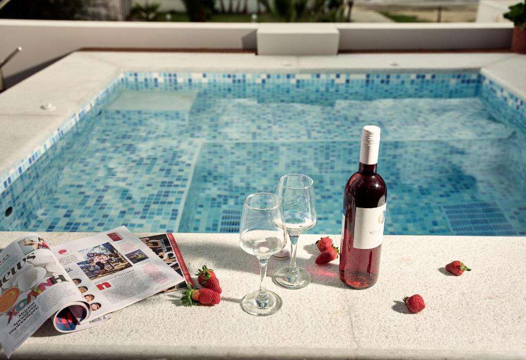 a bottle of wine and two glasses next to a swimming pool at Savvas Luxury Suites in Laganas
