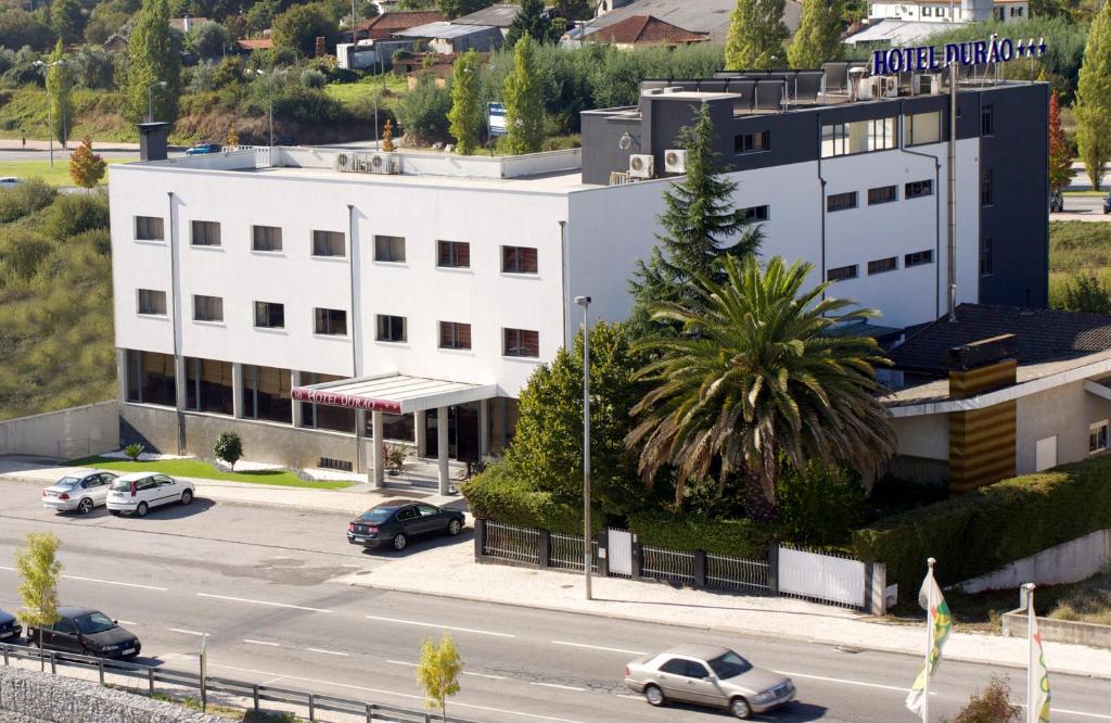 een wit gebouw met auto's geparkeerd op een parkeerplaats bij Hotel Durao in Viseu