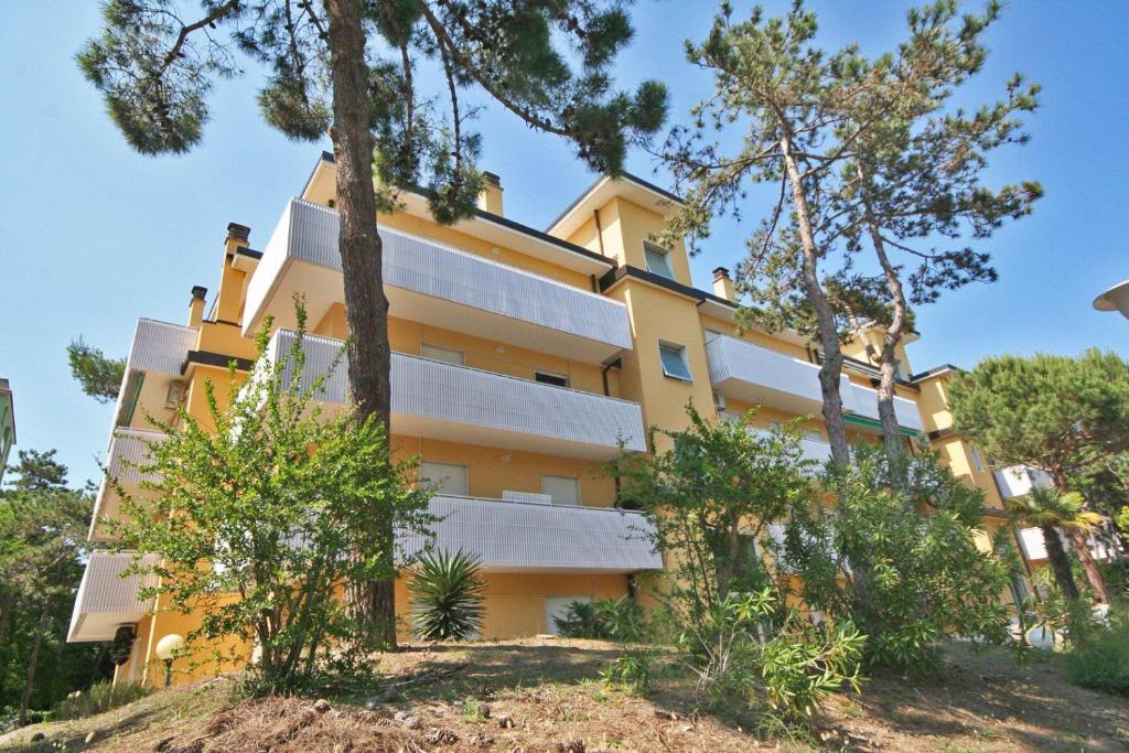 um edifício amarelo com árvores em frente em BA- Tintoretto Apartments - em Lignano Sabbiadoro
