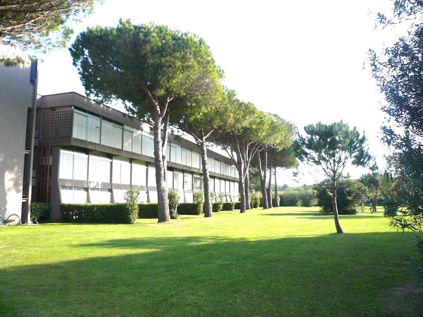 a building with trees in front of a grass field at Appartamenti Marina del Forte in Marina di Bibbona