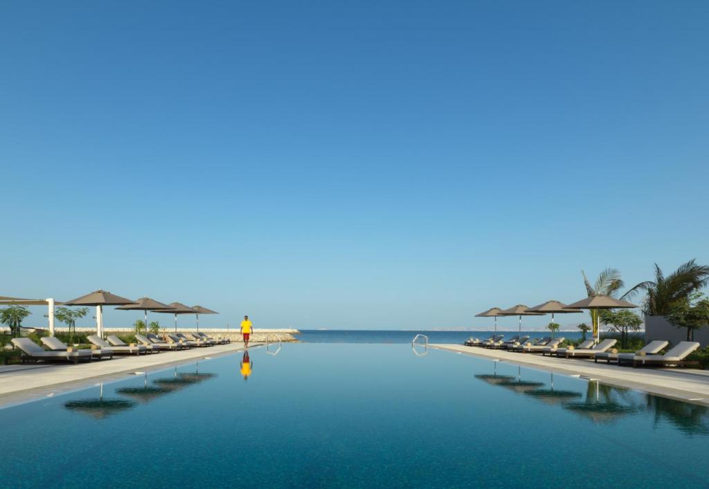 a pool with chairs and the ocean in the background at Kempinski Hotel Muscat in Muscat
