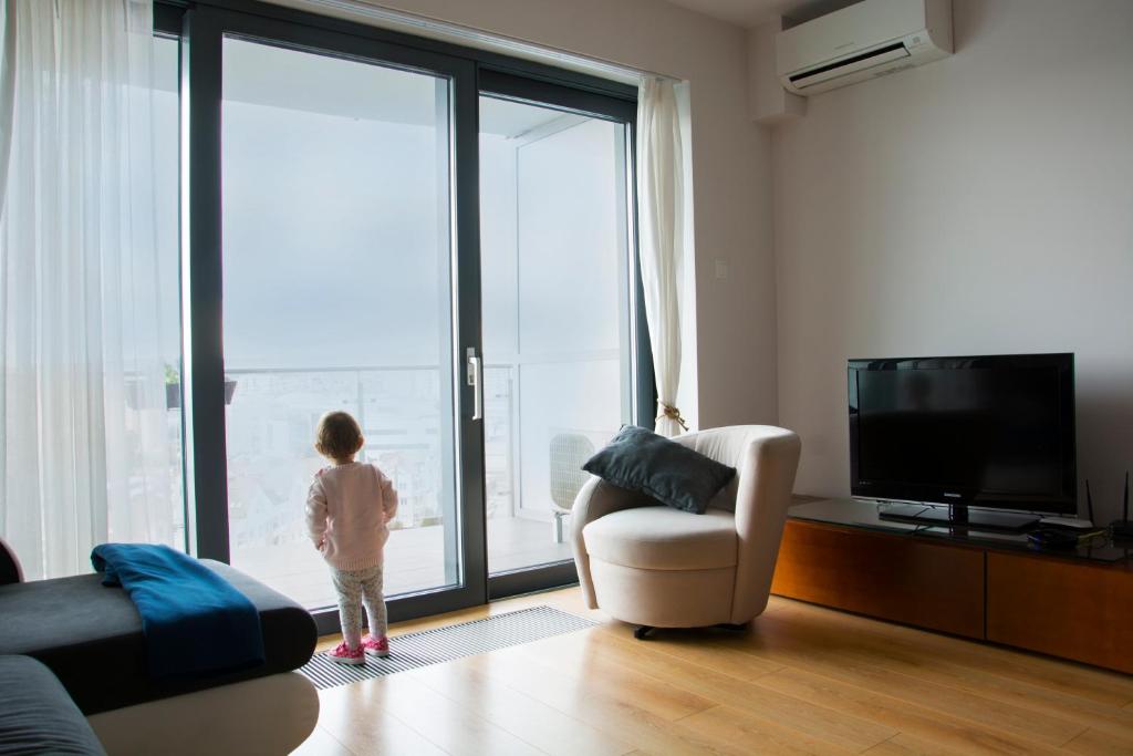 ジェシュフにあるKapart Rzeszów Apartmentの窓の外を見下ろすリビングルームに立つ小さな子供
