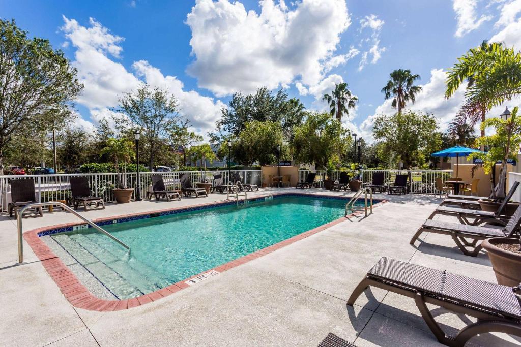 a swimming pool with chaise lounge chairs and trees at Baymont by Wyndham Fort Myers Airport in Fort Myers