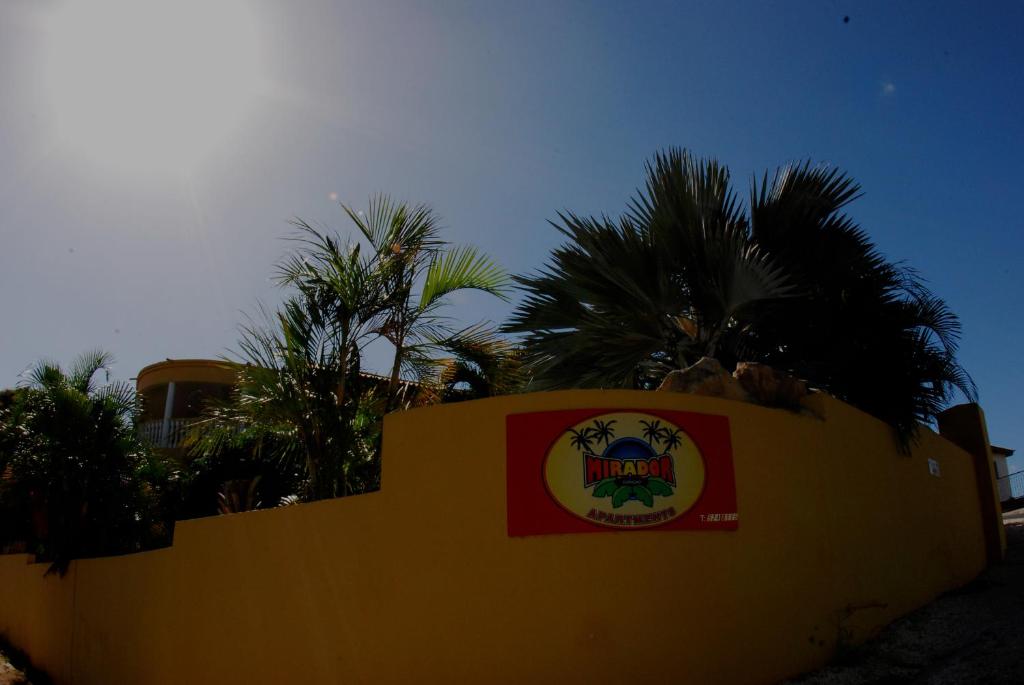a yellow wall with a sign on it with palm trees at Mirador Apartments in Willemstad