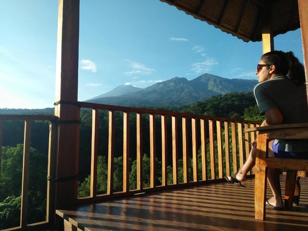 una mujer sentada en un banco en un porche mirando las montañas en Dragonfly Senaru Lodge, en Senaru