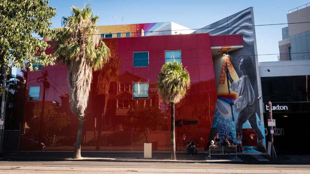 a red building with palm trees in front of it at Nomads St Kilda in Melbourne