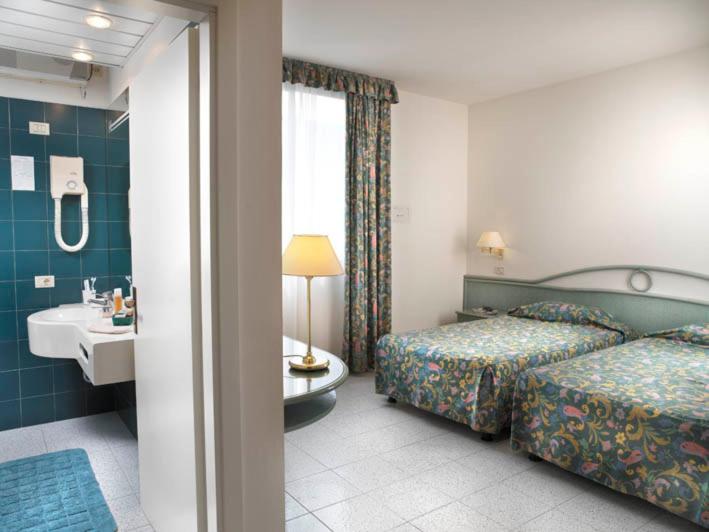 a hotel room with two beds and a sink and a bathroom at Hotel Italia in Bellaria-Igea Marina