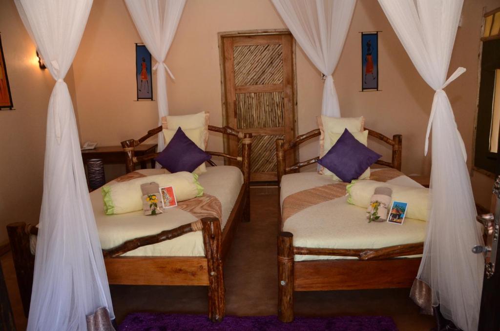 2 Betten in einem Zimmer mit Vorhängen und lila Kissen in der Unterkunft Hoima Cultural Lodge in Hoima