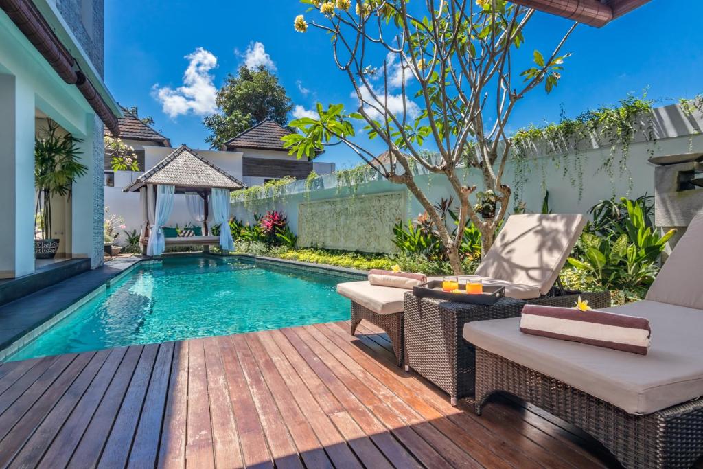 een zwembad in de achtertuin met een houten terras en een stoel en een tafel bij Villa Allamanda by Kubu GWK in Jimbaran