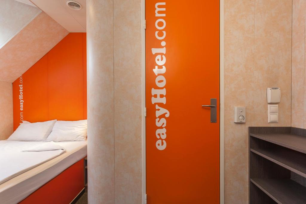 a small room with a bed and a orange door at easyHotel Budapest Oktogon in Budapest