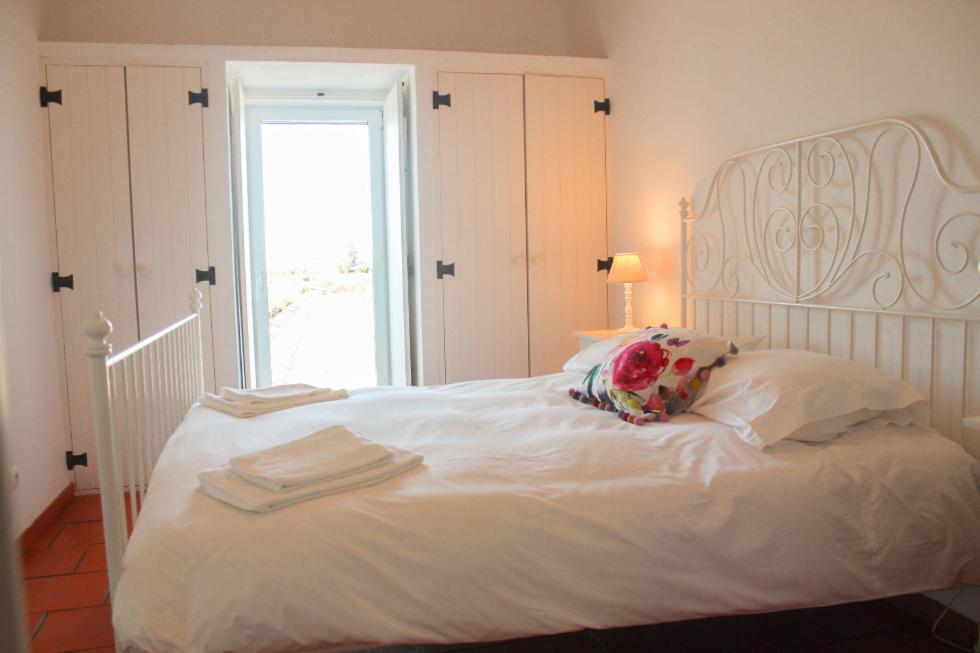 a white bed with a flower pillow and a window at Comporta House in Comporta