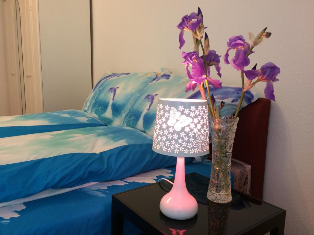 a table with a lamp and a vase with purple flowers at Írisz Apartman Budapest in Budapest