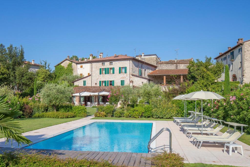 a swimming pool with chairs and an umbrella and a house at Antico Casale Bergamini in SantʼAmbrogio di Valpolicella