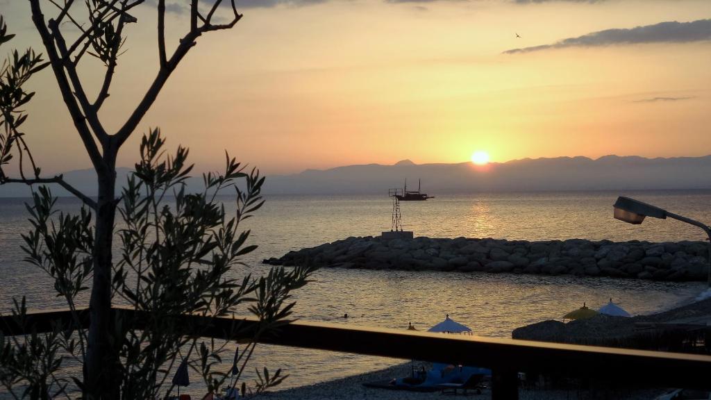 a sunset over the ocean with a boat in the water at Moireas Apartments in Akrogiali