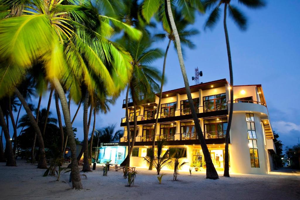 a building on the beach with palm trees at Kaani Beach Hotel in Maafushi