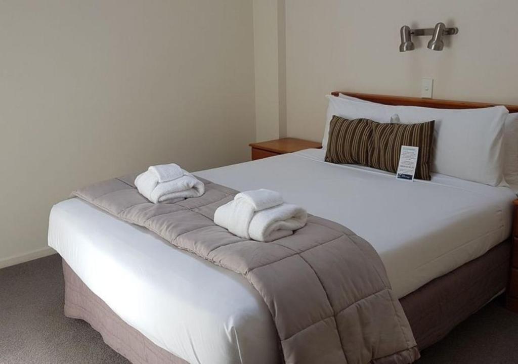 um quarto com uma grande cama branca com toalhas em Courtenay Village em Wellington