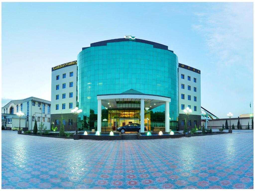 un gran edificio de cristal con un coche delante en Golden Valley Hotel, en Tashkent